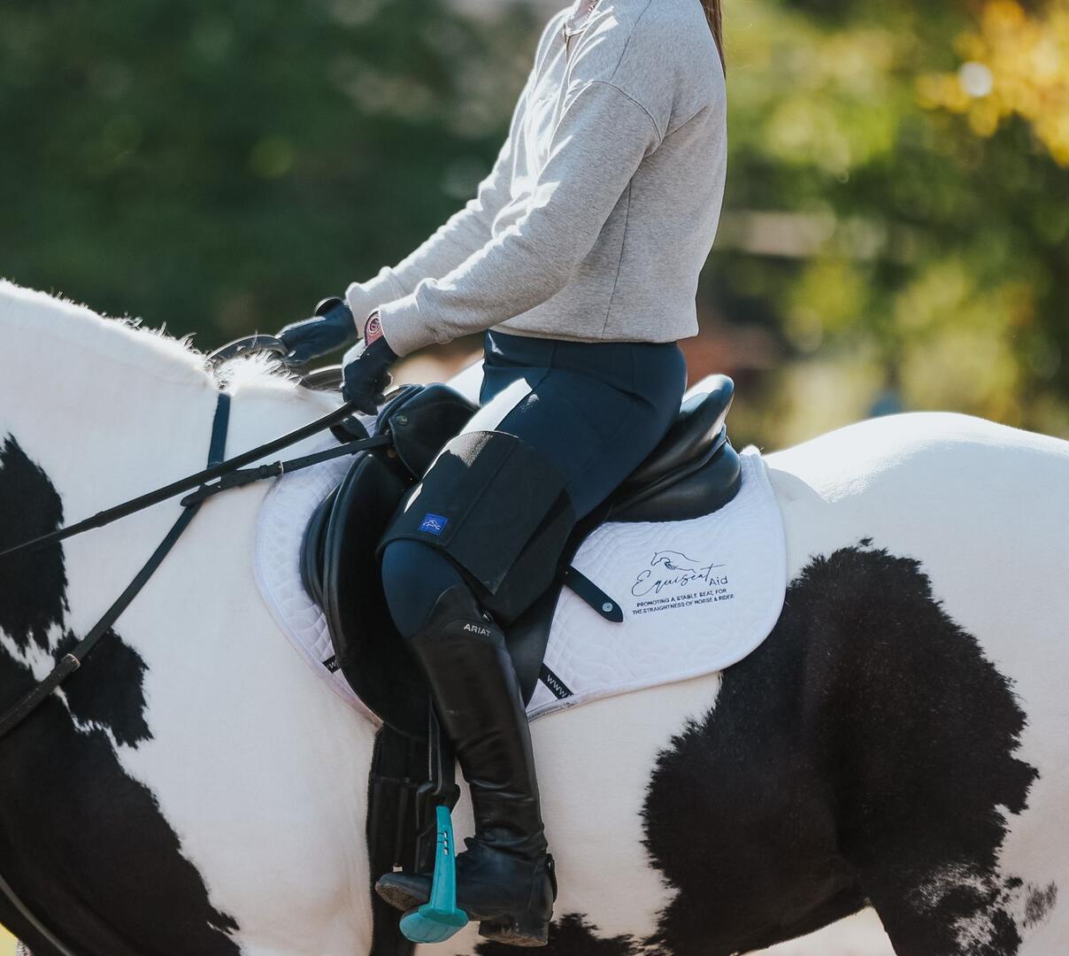Horse rider wearing their black Equiseat Aid on their left thigh, sat on a piebald horse, wearing an Equiseat Aid Saddle Pad